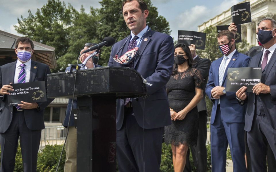 Congressman Crow speaks from behind a podium, surrounded by people