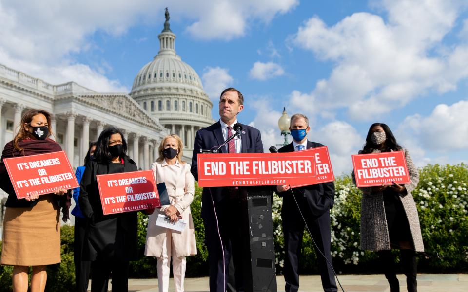 Rep. Crow speaking at a podium surrounded by Members of Congress